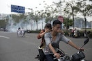 Residents cover their faces as they ride a motorcycle along a street after tear gas was released by police to disperse a protest against a chemical plant project in Maoming