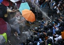 Protesters wearing raincoats and carrying umbrellas face pepper spray from riot police, as tens of thousands of protesters block the main street to the financial Central district outside the governmen