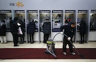 Customers use automated teller machines as a worker vacuums the floor at a branch of KB Kookmin Financial Group in Seoul