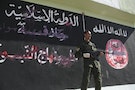 Kurdish Peshmerga fighter stands near a wall on which black flag commonly used by Islamic State militants and other writing have been painted over, in Zumar