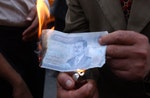 在獲知Hussein被捕後，一名伊拉克民眾燒毀上有Saddam Hussein頭像的紙幣。Photo Credit: AP/達志影像 