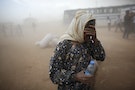 A Kurdish Syrian refugee covers her face as she waits for transport during a sand storm on the Turkish-Syrian border near the southeastern town of Suruc