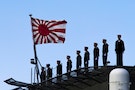 Sailors stand on the deck of the Izumo warship as it departs from the harbour of the Japan United Marine shipyard in Yokohama