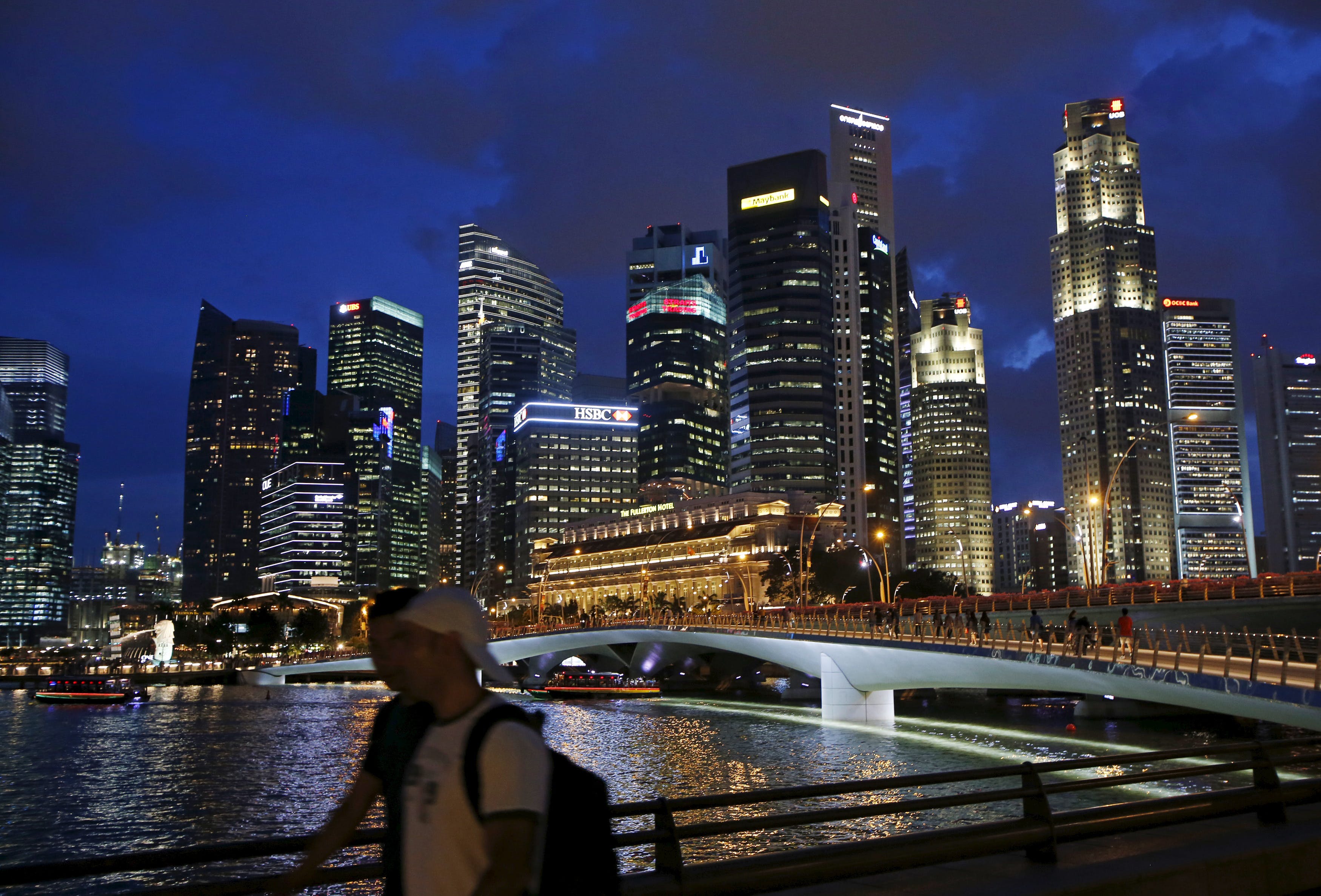 People walk past the skyline of the central business district in Singapore