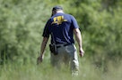 A federal agent stretches yellow crime tape across a field for Hoffa investigation in Oakland Township, Michigan