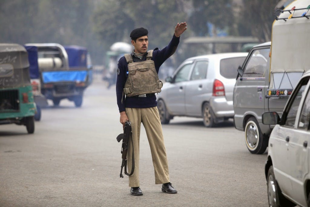A policeman raises his hand to stop a car for a security check on a road in Peshawar