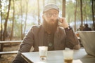 Germany, Berlin, beared man sitting in a garden cafe using smartphone