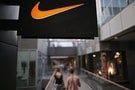 People walks past a Nike shop under the company logo at the Sanlitun shopping area in central Beijing