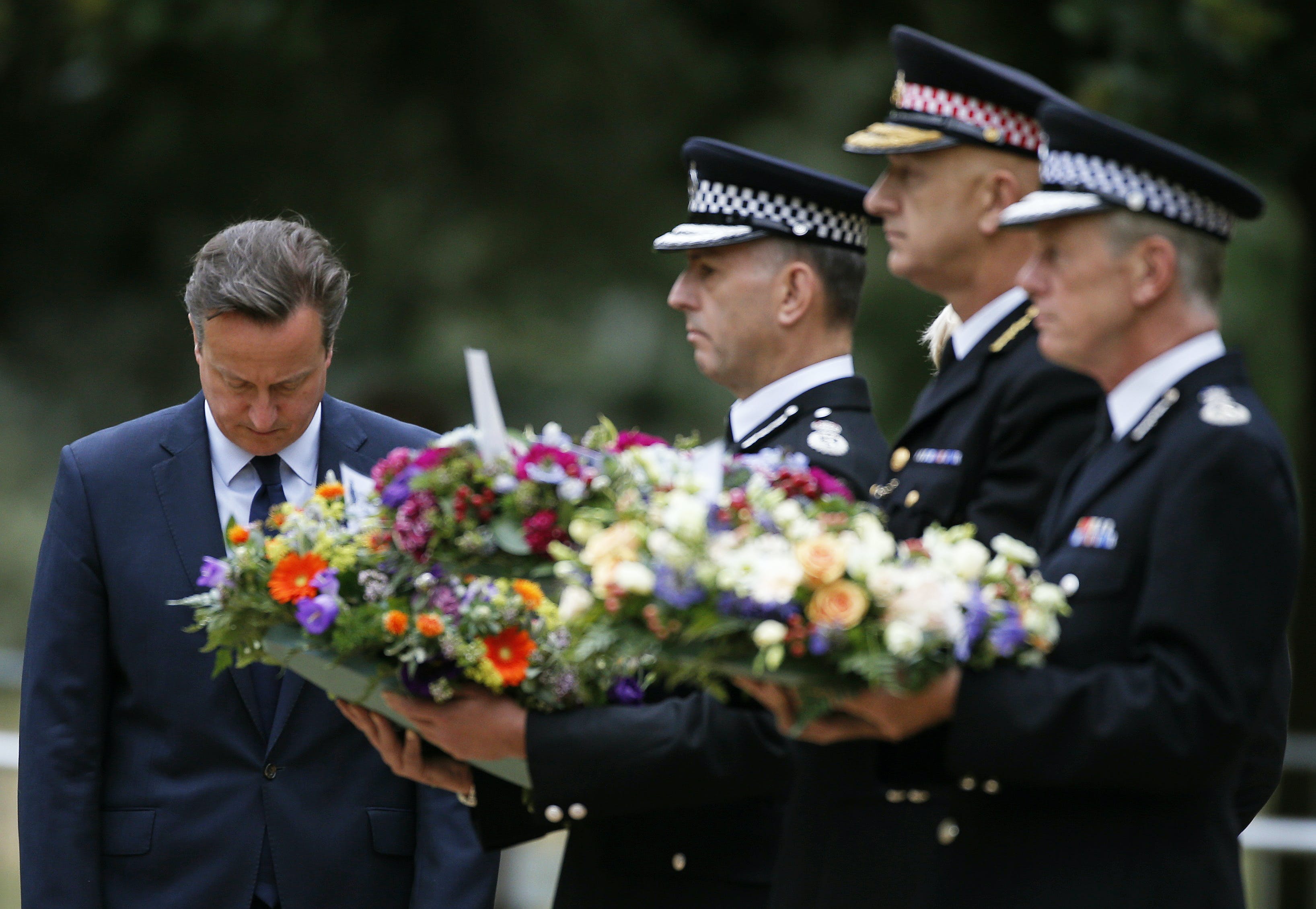 Britain's Prime Minister David Cameron bows as he stands with police officers after laying a wreath at the memorial to victims of the July 7, 2005 London bombings