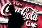 Pedestrian passes large Coca-Cola sign in eastern Sydney.