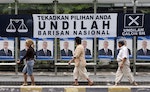 Peope walk past a bus stop decorated with election posters and banner in Kuala Lumpur