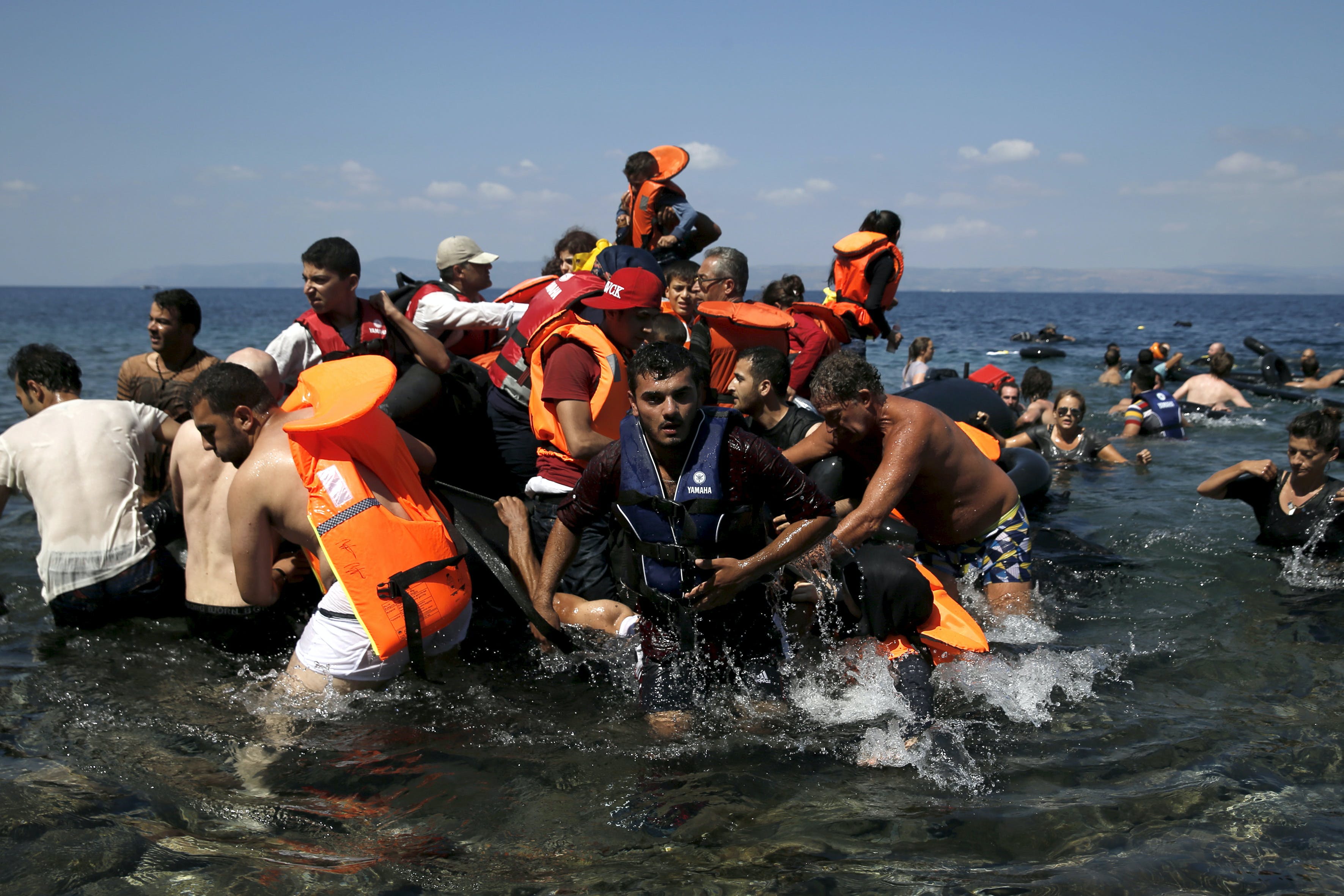 Syrian and Afghan refugees are helped by locals and volunteers as they reach the shore after their dinghy deflated some 100m away from the Greek island of Lesbos