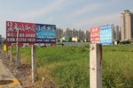 單元二重劃區内大型建案廣告看板豎立於雜草叢生的土地上（作者於2015年7月所拍攝）