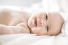 Baby lying on bed smiling at camera