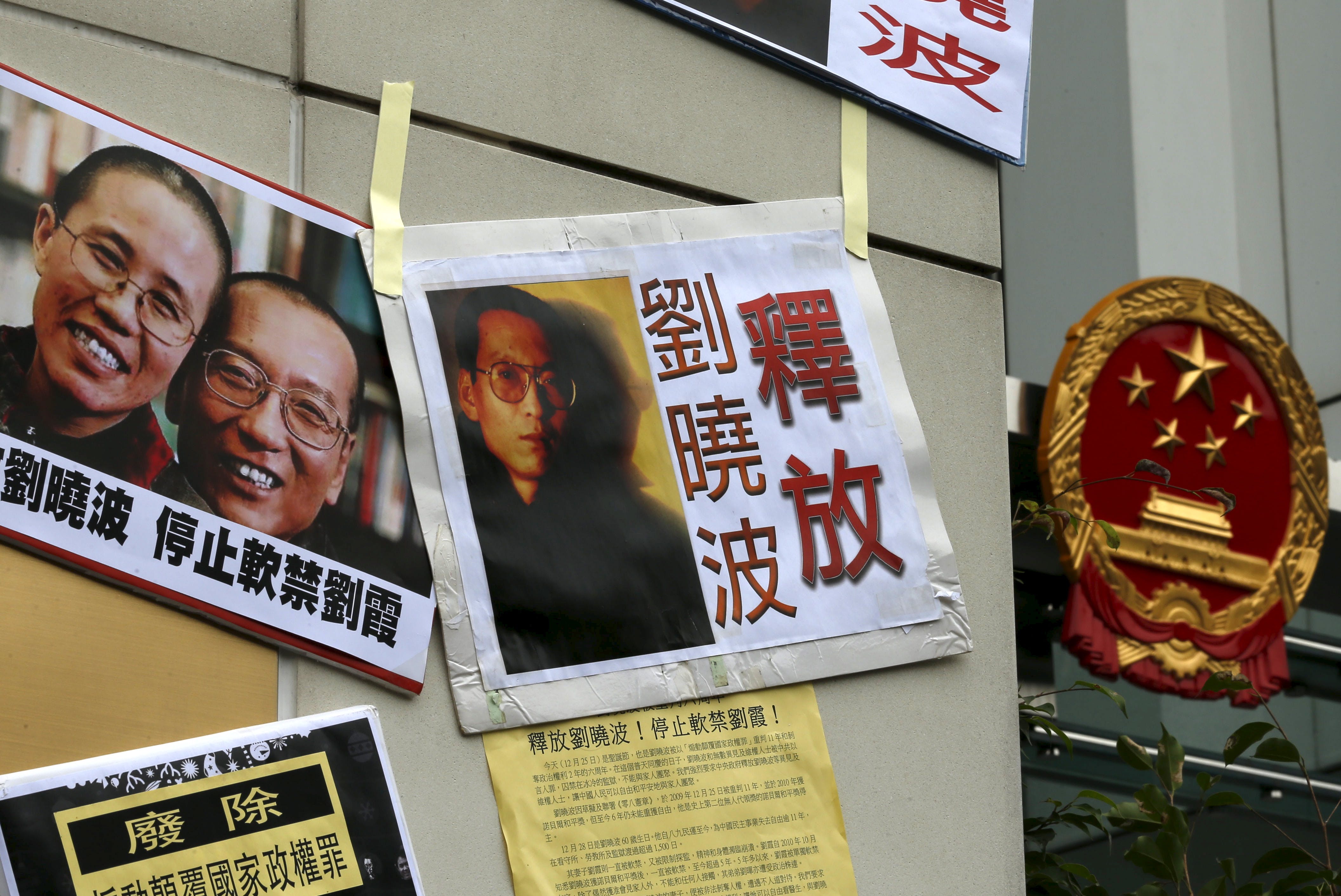 Signs and portraits of jailed Chinese Nobel Peace Prize laureate Liu Xiaobo and his wife Liu Xia are seen in front of the national emblem of China during a protest outside the Chinese liaison office i