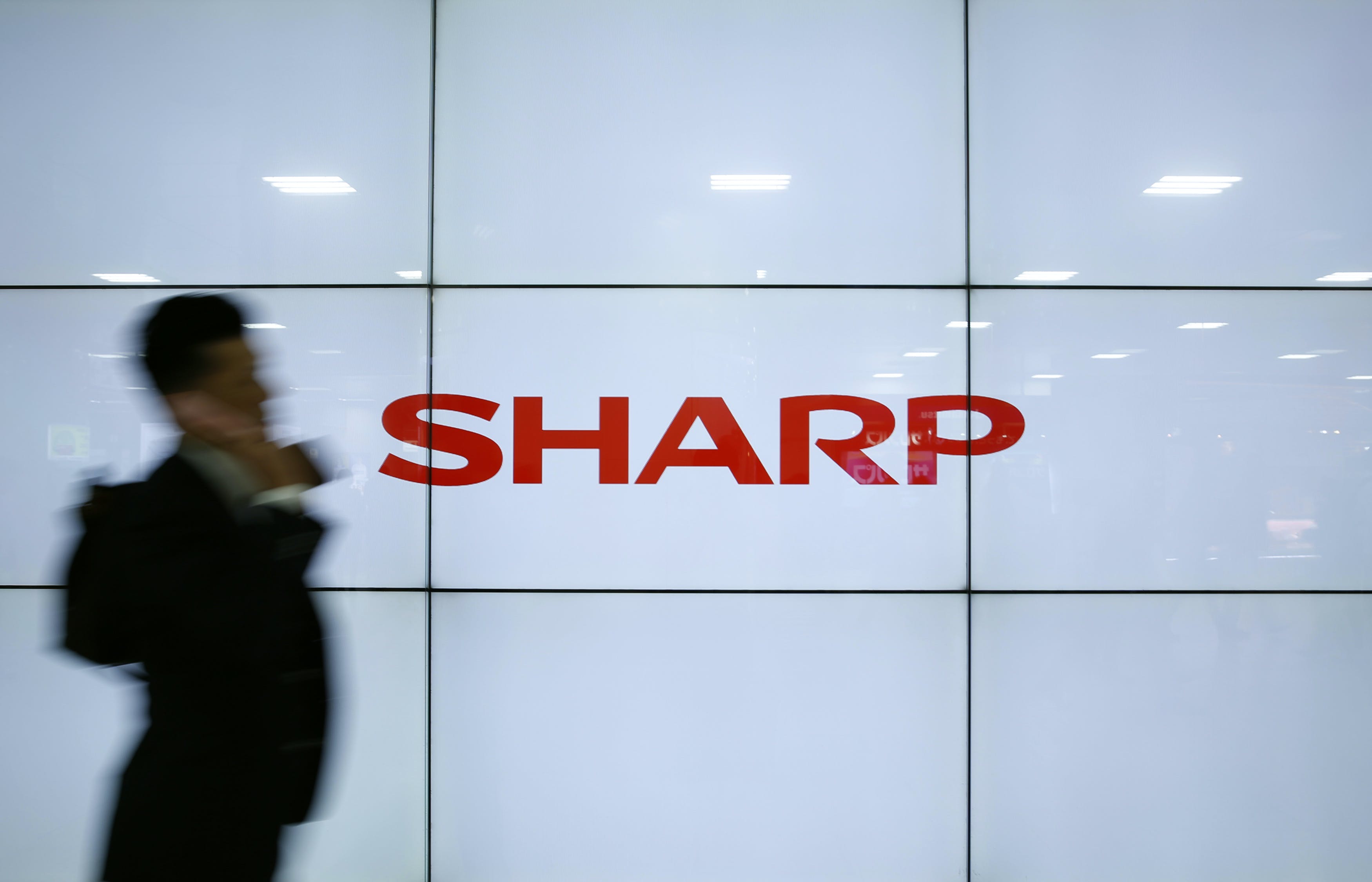 夏普＿A man using his mobile phone walks past Sharp Corp's liquid crystal display monitors showing the company logo in Tokyo