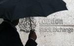 A man shelters under an umbrella as he walks past the London Stock Exchange