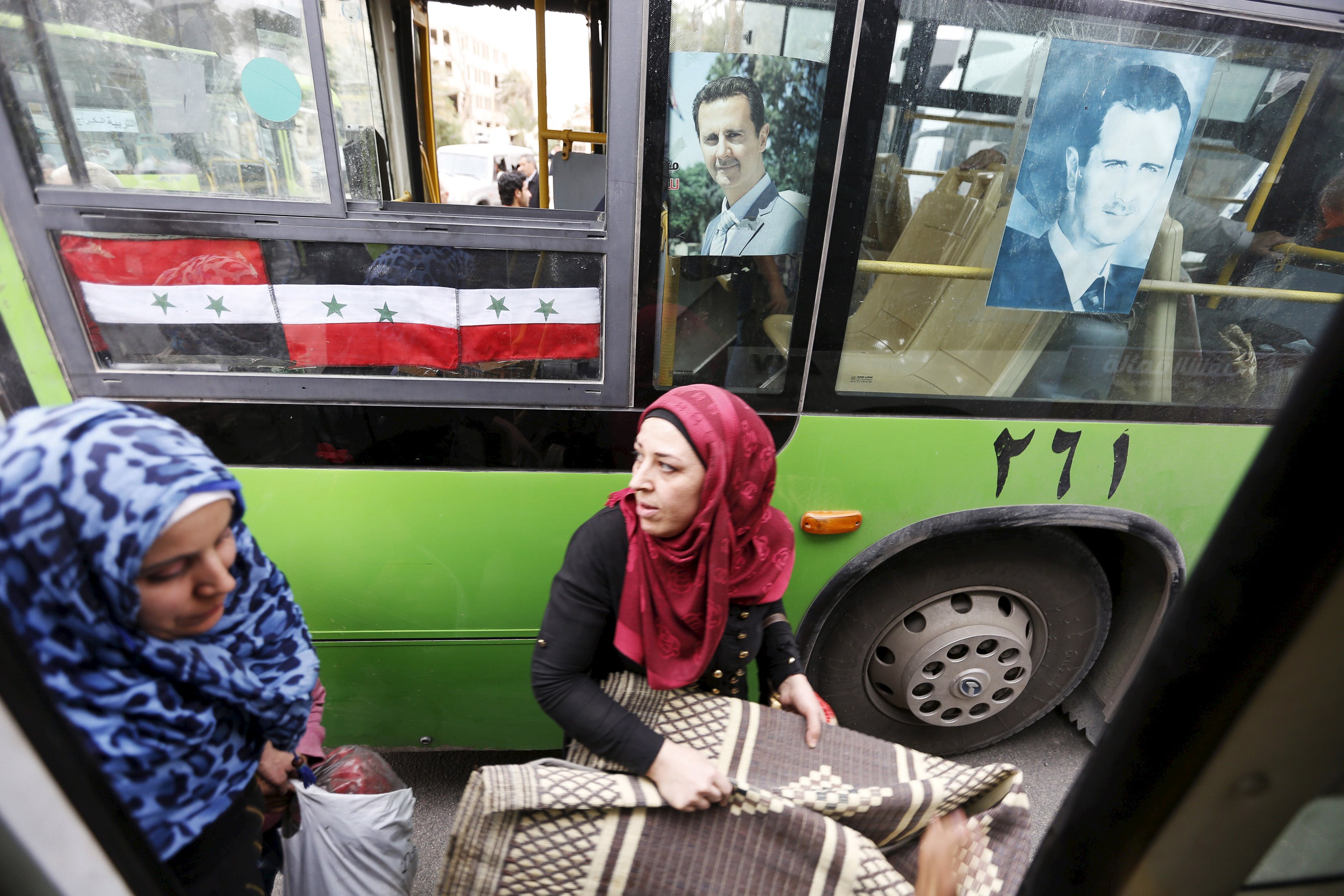 Women carry belongings they collected from their damaged houses as they get into into a bus after their visit to the city of Palmyra