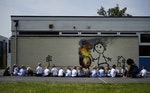 Reception class school children sit in a row as they draw a mural attributed to Banksy in Bristol