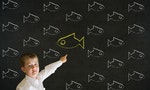 Pointing boy dressed up as business man with independent thinking chalk fish swimming against the flow on blackboard background