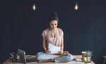 Focused african american businesswoman sitting in lotus pose with papers on table with laptop in office — Photo by alebloshka