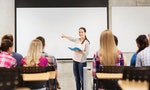 education, high school, teamwork and people concept - smiling student girl with notebook standing and pointing finger in front of students in classroom