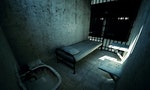 Render of locked old prison cell for one person with bed, sink, toilet and chair. Dark atmosphere.