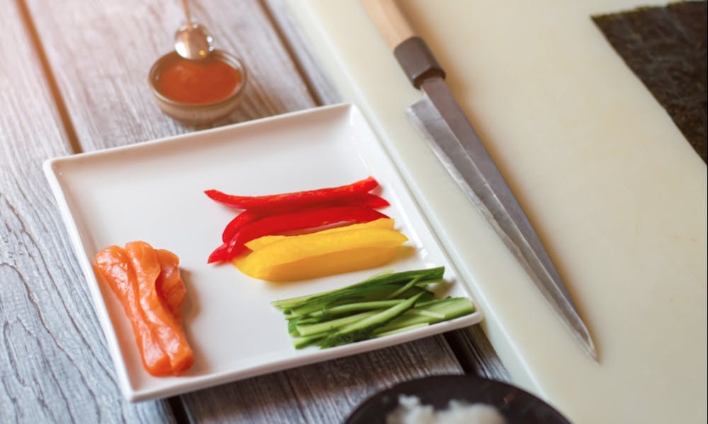 Raw fish and sliced paprika. Knife beside plate with vegetables. Fresh ingredients for sushi rolls. Pieces of ripe bell pepper.