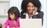 Beautiful middle aged African American woman or businesswoman working on her cell phone & laptop computer and looking after her female child daughter