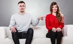 Shy woman and man sitting on sofa couch next each other. First date. Attractive girl and handsome guy meeting dating and trying to talk. Male touching picking up female.