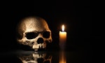 Death concept. One human skull near lighting candle on dark background