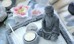 Grey stone buddha in front of a small yellow candle on a zen table