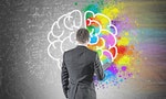 Rear view of a young businessman in a gray suit holding a folder. He is looking forward. A blackboard with a colorful brain sketch