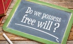Do we possess free will? A question in white chalk on a vintage blackboard with a stack of books against rustic wooden table - 圖片