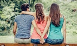 Love triangle, a girl is hugging a guy and he is holding hands with another girl, they are sitting together on a bench - 圖片