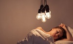 A girl lies in bed under big light bulbs can't fall asleep. Concept picture. Insomnia. Psychology.