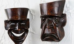 幸災樂禍 Schadenfreude  Sad tragedy theatre mask on plaster wall with laughing comedy mask in the background
