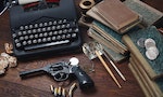 Writing a detective story - old retro vintage typewriter and revolver gun with ammunitions, books, papers, old ink pen on wooden table