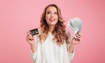 Photo of happy young woman standing isolated over pink background. Looking aside holding money and credit card.
