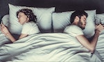 Young couple in bed using phone lying backs to each other.
