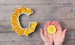 Vitamin C nutrient in food concept. Plate in shape of letter C with orange slices and woman hand with citrus on wooden background. Flatlay. Ascorbic acid is important for immune system function.