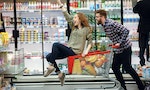 Happy couple having fun while choosing food in the supermarket. Young happy man pushing shopping cart with his girfriend inside