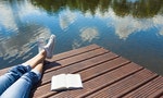 Relaxing holiday by the lake. Woman's feet relaxing on a wooden dock with book at her side.