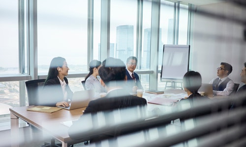 through-the-glass shot of a team of asian business people meeting in company conference room