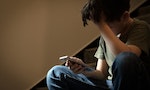 Cyber bullying concept. Young Asian preteen/teenage boy sitting at stair, covering his face with hand, other hand holding smartphone. Alone, stressed, frustrated, overwhelmed, crying, depressed, tech.