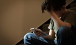 Cyber bullying concept. Young Asian preteen/teenage boy sitting at stair, covering his face with hand, other hand holding smartphone. Alone, stressed, frustrated, overwhelmed, crying, depressed, tech.