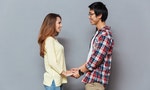 Young happy couple looking at each other and holding hands isolated on the gray background